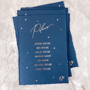 May include: A stack of dark blue cards with gold foil lettering. The cards have a star and crescent moon design. The text on the cards reads "Polaris" and lists names including Leticia Ritchie, Ben Ritchie, Callie Ritchie, Amanda Baker, Ian Baker, Melanie Ritchie, and Chris Ritchie.
