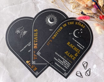 May include: Three arch-shaped black wedding invitation cards with gold foil text and celestial graphics. The cards feature the text "IT'S WRITTEN IN THE STARS," "RACHEL & ALICE," and "THE DETAILS." Includes moon, star, and hand illustrations.