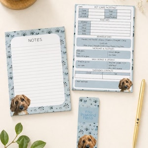 May include: A pet care notepad set with a light blue paw print design. The set includes a notepad, a pet care notepad, and a bookmark. Each item features a photo of a dog. A gold pen is also included.