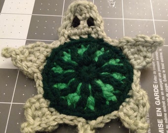 May include: A crocheted turtle with a green shell and gray body. The turtle has black eyes and a simple design.