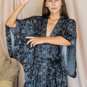 May include: A woman wearing a blue and white floral print kimono with long sleeves and a sash. She is wearing gold necklaces.