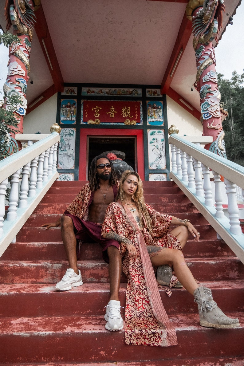 Puede incluir: Una pareja vestida con t&uacute;nicas rojas y doradas posa en los escalones de un templo chino tradicional. El templo tiene un techo rojo y paredes blancas con intrincados tallados y pinturas. La pareja est&aacute; sentada en los escalones, la mujer a la derecha y el hombre a la izquierda. La mujer tiene el pelo largo y rubio y lleva una t&uacute;nica roja y dorada con una larga cola. El hombre tiene el pelo largo y negro y lleva una t&uacute;nica roja y dorada con una cola corta. El templo est&aacute; decorado con s&iacute;mbolos y caracteres chinos tradicionales. El texto en el templo dice "高音 韻".