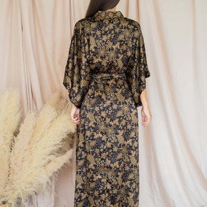 May include: A black and gold floral print kimono-style robe with a matching belt. The long robe features a shawl collar and wide sleeves. The fabric has a shiny finish and a detailed botanical pattern.