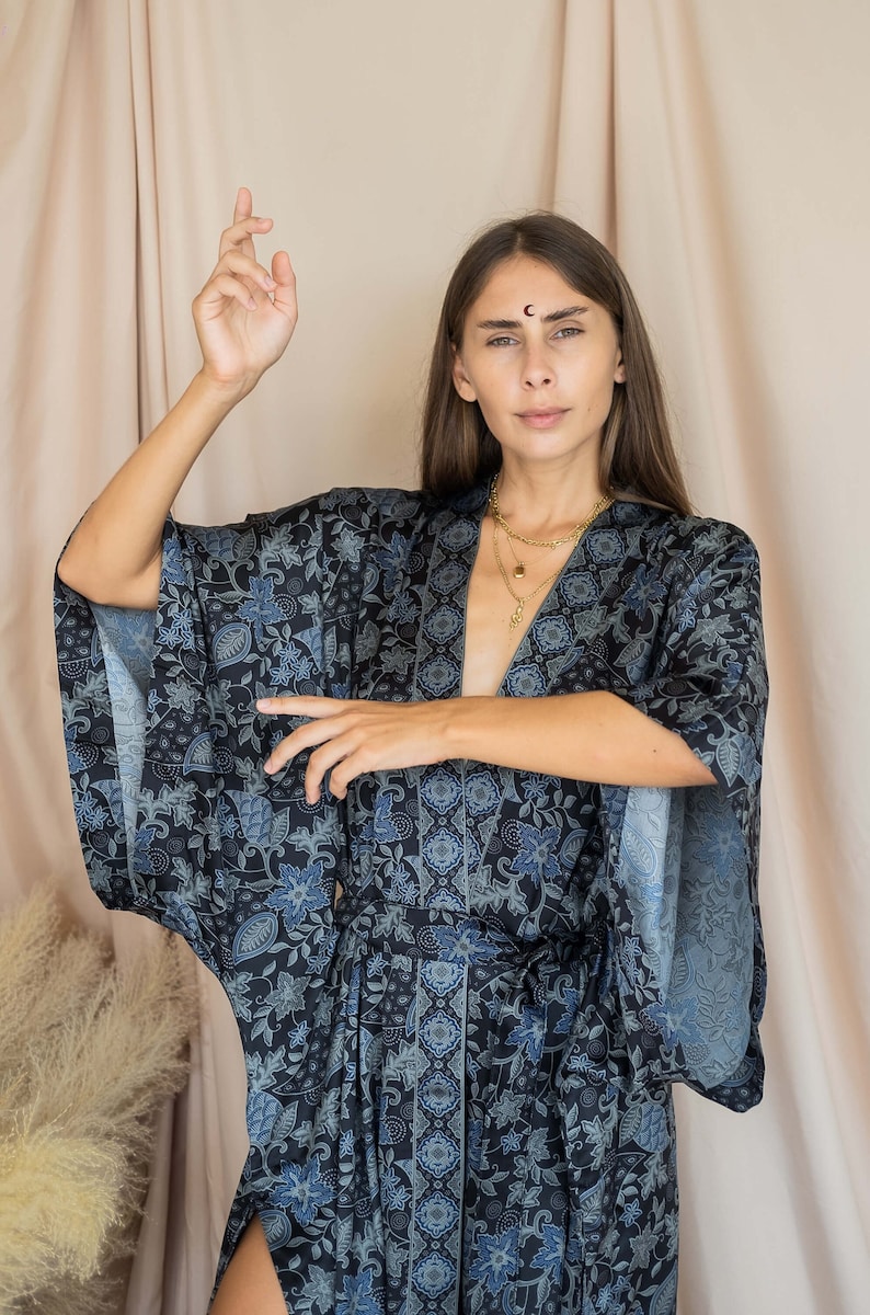 May include: A woman wearing a blue and white floral print kimono with long sleeves and a sash. She is wearing gold necklaces.