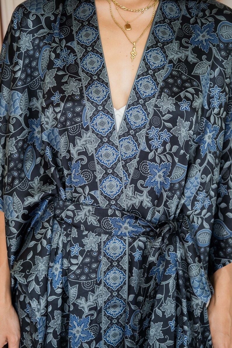 May include: A black and blue patterned silk robe with a tie belt. The robe features a floral design with a geometric border.