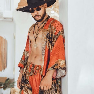 May include: A person wearing a black hat, sunglasses, and a red and gold patterned kimono. They are also wearing a necklace with a large gold pendant.
