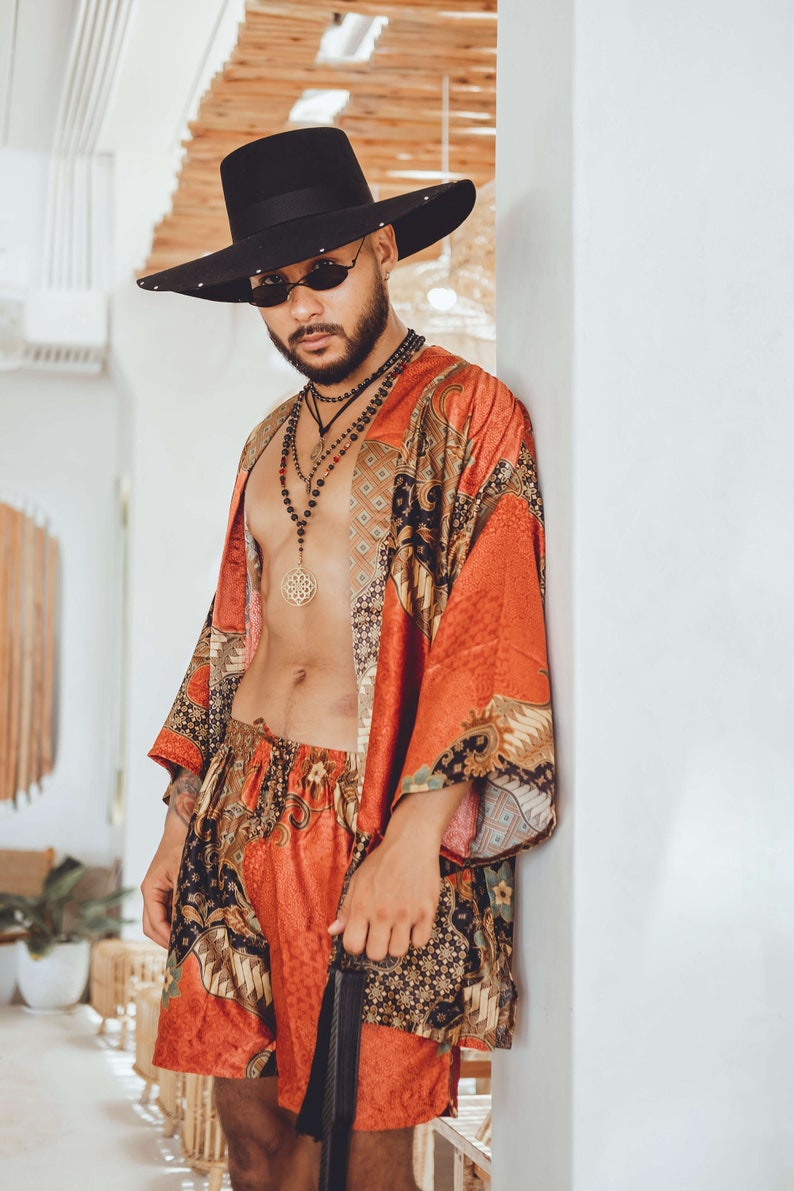 May include: A person wearing a black hat, sunglasses, and a red and gold patterned kimono. They are also wearing a necklace with a large gold pendant.