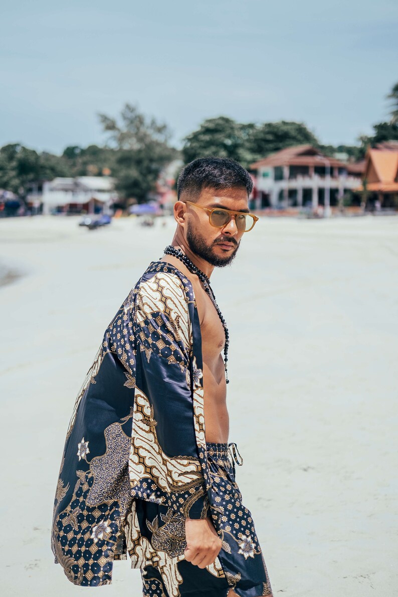 May include: A man wearing a black and gold patterned kimono with a beaded necklace. He is wearing sunglasses and has a beard.