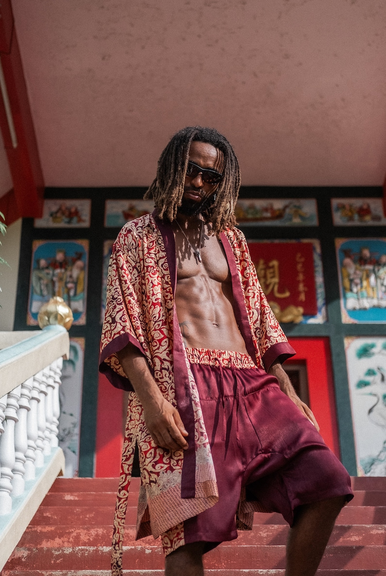 May include: A person wearing a red and gold patterned robe with a burgundy satin shorts. The person is standing on a set of stairs in front of a building with colorful decorations.