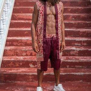 May include: A man wearing a red and gold patterned sleeveless shirt and matching shorts. He is standing on a set of red stairs and wearing white sneakers.