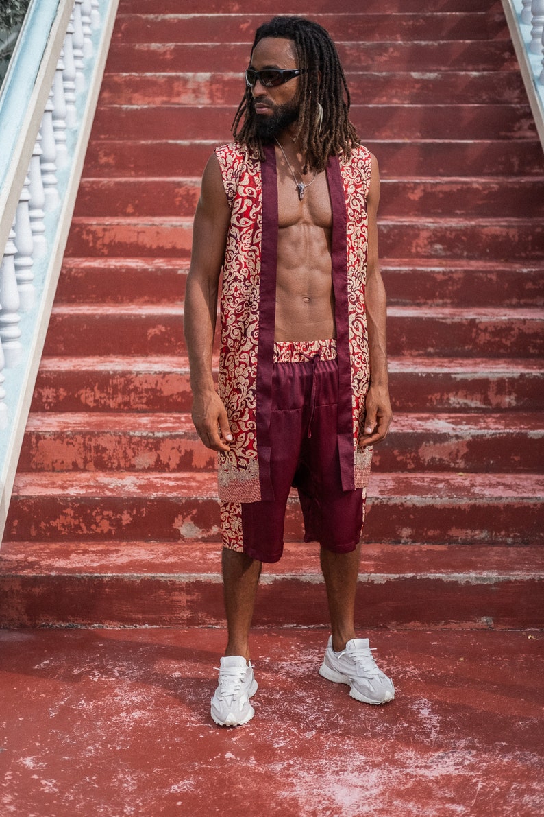 May include: A man wearing a red and gold patterned sleeveless shirt and matching shorts. He is standing on a set of red stairs and wearing white sneakers.
