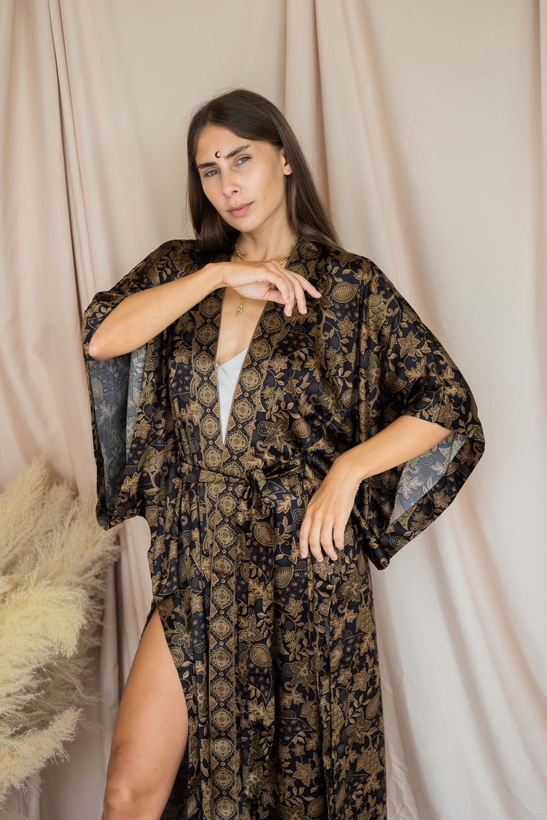 May include: A black and gold patterned kimono robe with a matching belt. The robe features a floral design and a high slit on the side. The sleeves are wide and flowing, and the fabric appears to be silky.
