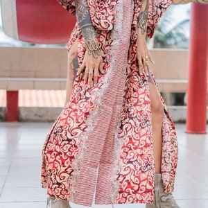 Puede incluir: Una bata de kimono de patr&oacute;n rojo y dorado con una silueta larga y fluida. La bata tiene un lazo de cintur&oacute;n y una abertura lateral. La modelo lleva la bata con un par de botines beige.