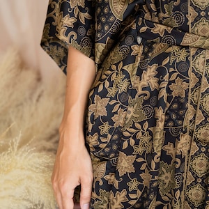 May include: A black kimono-style robe with a floral pattern in shades of brown and olive green. The robe features a wrap-around design with a belt and wide sleeves. The fabric has a silky sheen.