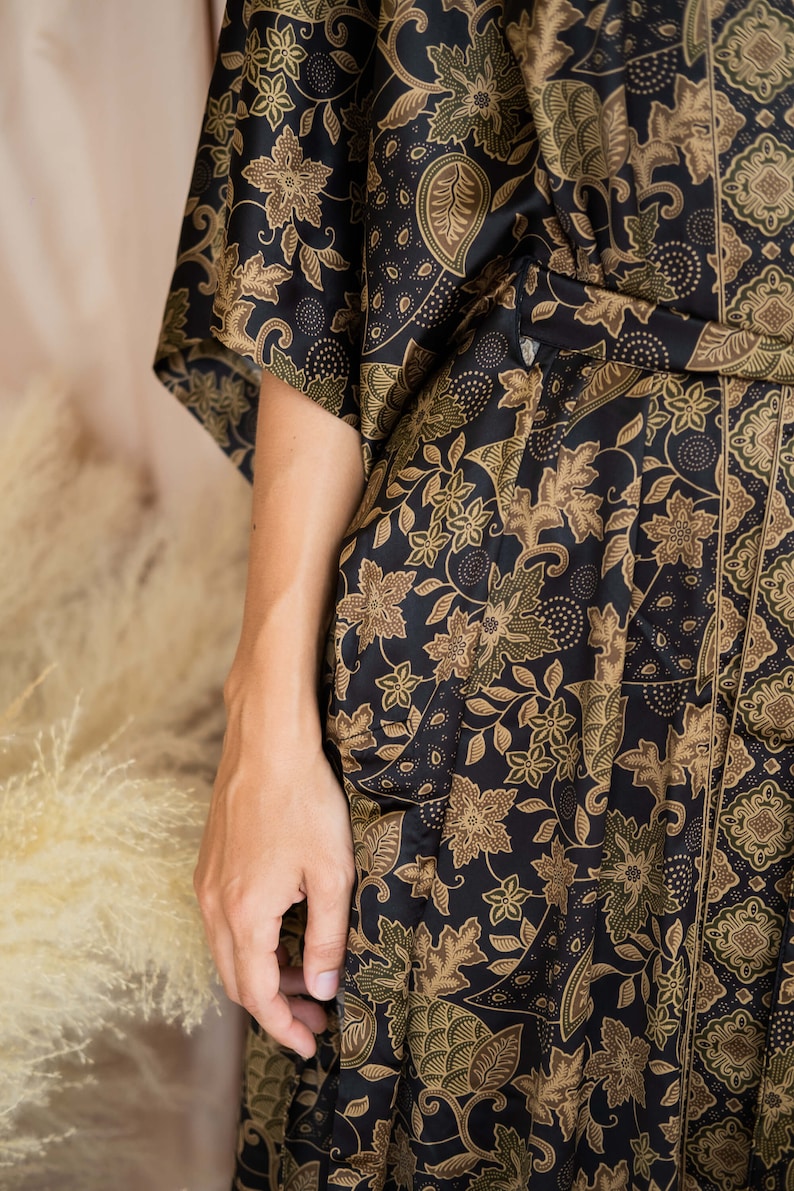 May include: A black kimono-style robe with a floral pattern in shades of brown and olive green. The robe features a wrap-around design with a belt and wide sleeves. The fabric has a silky sheen.
