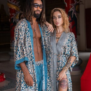 May include: Two people wearing matching blue and gold patterned robes. The man is wearing sunglasses and has dreadlocks. The woman has long blonde hair and is wearing a gold necklace.