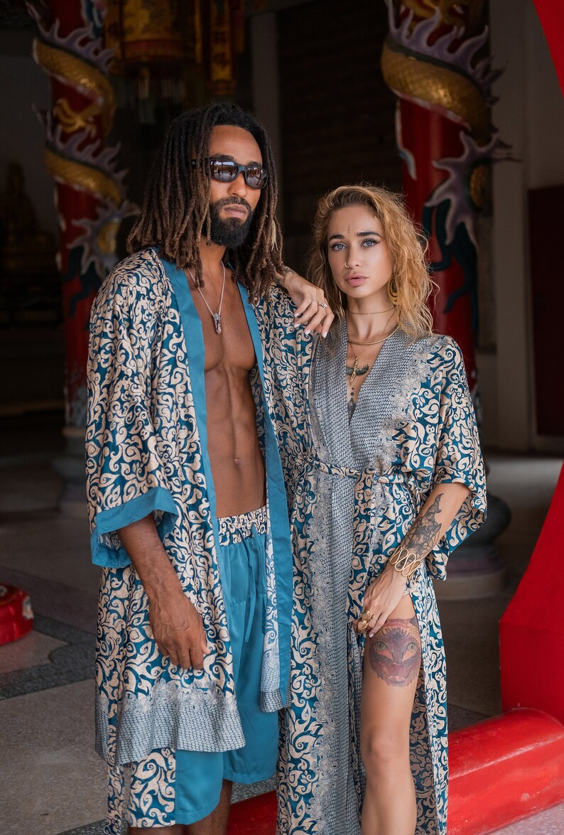 May include: Two people wearing matching blue and gold patterned robes. The man is wearing sunglasses and has dreadlocks. The woman has long blonde hair and is wearing a gold necklace.