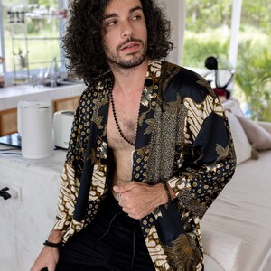 May include: A black and gold patterned kimono-style robe with a floral and geometric design. The robe is worn with black shorts and a black beaded necklace. The overall aesthetic is bohemian and relaxed.