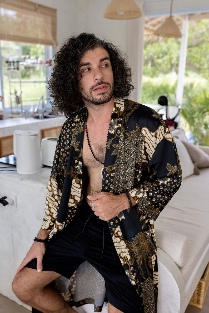 May include: A black and gold patterned kimono-style robe with a floral and geometric design. The robe is worn with black shorts and a black beaded necklace. The overall aesthetic is bohemian and relaxed.