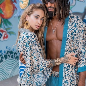 May include: A couple wearing matching blue and cream patterned robes. The woman is wearing large gold hoop earrings. The man has dreadlocks and is wearing sunglasses.