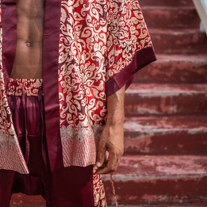 May include: A burgundy silk robe with a gold and red floral pattern. The robe has a long sleeve and a sash tie.