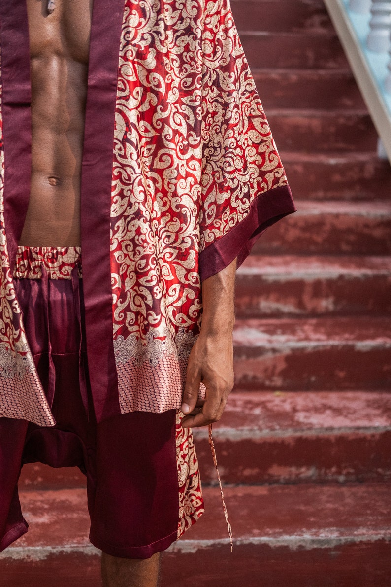 May include: A burgundy silk robe with a gold and red floral pattern. The robe has a long sleeve and a sash tie.