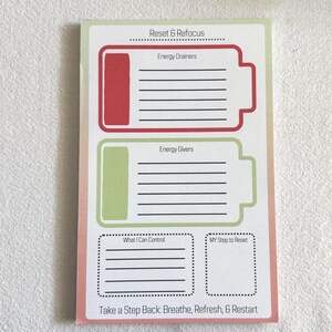 May include: A rectangular notepad with a pink and green border. The notepad features sections labeled "Reset & Refocus," "Energy Drainers," "Energy Givers," "What I Can Control," and "My Step to Reset." The text "Take a Step Back: Breathe, Refresh, & Restart" is at the bottom.
