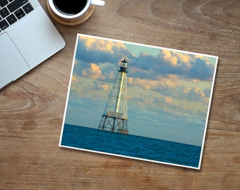 May include: A white and black lighthouse stands tall against a blue sky with fluffy white clouds. The lighthouse is in the middle of the ocean with blue water.