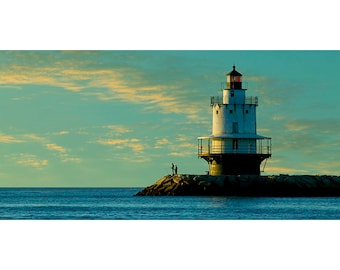 May include: A white lighthouse with a red light on top, standing on a rocky island in the ocean. The sky is a light blue with yellow clouds. Two people are fishing on the rocks in the foreground.