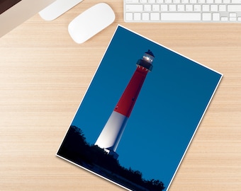 May include: A red and white lighthouse with a light on top against a blue sky at night.