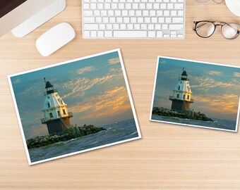 May include: A white and black lighthouse with a red roof stands on a rocky outcropping in the ocean. The sky is a mix of blue and orange with clouds.