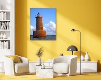May include: A rusty brown lighthouse stands tall against a blue sky with white clouds. The lighthouse is located in the middle of a body of water.