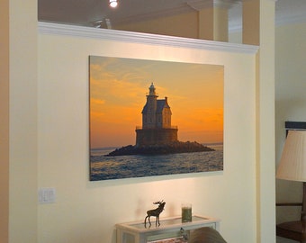 May include: A framed photograph of a lighthouse on a small island at sunset. The lighthouse is a white building with a red roof and a black lantern. The water is a deep blue and the sky is a vibrant orange and pink.