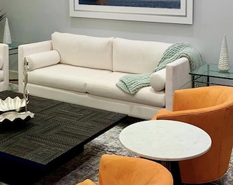 May include: A living room interior with a white sofa, two orange armchairs, a black coffee table, and a framed photograph of a lighthouse on a body of water.