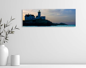 May include: A panoramic photograph of a white lighthouse on a rocky island with a blue sky and ocean in the background.