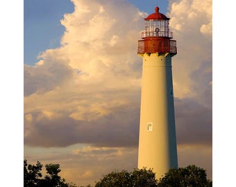 May include: A white lighthouse with a red roof and a red railing stands tall against a cloudy sky. The lighthouse is surrounded by green trees.