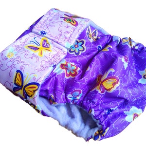 Puede incluir: Una cubierta de pañal para bebé con un estampado de mariposas y flores. La cubierta está hecha de tela morada y morada clara. El diseño de mariposa incluye acentos amarillos, azules y blancos. El interior es de un material azul claro.