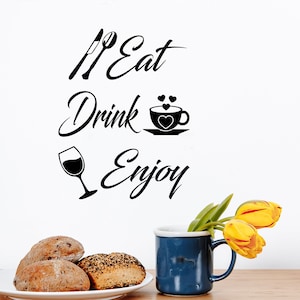 May include: Black and white kitchen wall decal with the text "Eat Drink Enjoy" with a fork and knife, a cup of coffee with hearts, and a glass of wine.