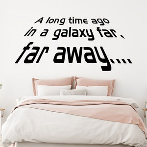May include: A bedroom with a white bed and pink bedding. The wall behind the bed has a black vinyl decal with the text "A long time ago in a galaxy far, far away..."