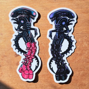 Może przedstawiać: Dwa czarne i białe naklejki z kosmitami w stylu science fiction. Jeden kosmita ma na sobie różowe buty, a drugi czarne buty.