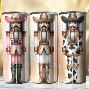 Op de afbeelding: Drie hoge, cilindrische bekers met cowboy notenkraker ontwerpen. Elke beker toont een andere cowboy notenkraker in roze, bruin en zwart, met cowboyhoeden en -laarzen. De tekst "6 BONUS DESIGNS INCLUDED!" is zichtbaar.