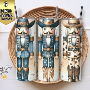 May include: Three tumbler cups with cowboy nutcracker designs. Each tumbler features a different cowboy nutcracker design in blue, brown, and cowhide patterns. The cups have black straws and are displayed in a woven basket.