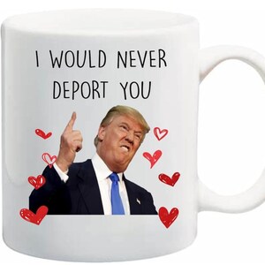 Könnte beinhalten: Weiße Keramik-Tasse mit gebogenem Henkel. Die Tasse zeigt den Text "I WOULD NEVER DEPORT YOU" über einem Bild eines Mannes im Anzug mit roten Herzillustrationen. Der Mann zeigt nach oben.