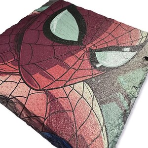 K&ouml;nnte beinhalten: Eine quadratische, strukturierte Schieferplatte mit einem Nahaufnahme von Spider-Mans Gesicht. Das Kunstwerk zeigt die Maske der Figur mit roten und schwarzen Netzdetails vor einem Hintergrund aus T&uuml;rkis- und Graut&ouml;nen.