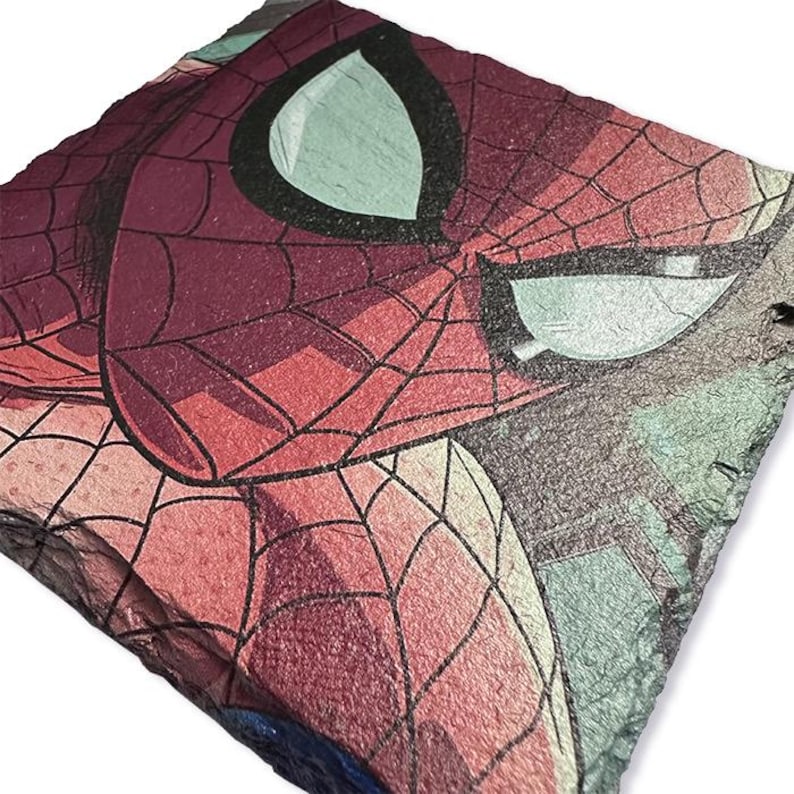 K&ouml;nnte beinhalten: Eine quadratische, strukturierte Schieferplatte mit einem Nahaufnahme von Spider-Mans Gesicht. Das Kunstwerk zeigt die Maske der Figur mit roten und schwarzen Netzdetails vor einem Hintergrund aus T&uuml;rkis- und Graut&ouml;nen.