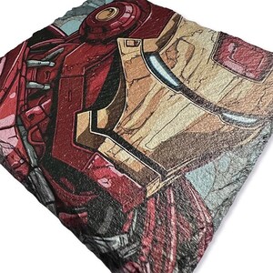 K&ouml;nnte beinhalten: Ein quadratischer Untersetzer aus Schiefer mit einer detaillierten Illustration von Iron Mans Helm und Schulterpanzerung. Das Kunstwerk verwendet Farbt&ouml;ne von Rot, Gold und Grau im Comic-Stil.