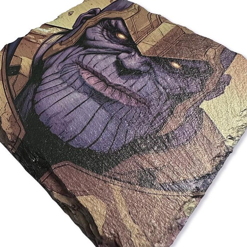K&ouml;nnte beinhalten: Ein quadratischer, strukturierter Steinuntersetzer mit einer Comic-Illustration von Thanos. Das Bild zeigt Thanos' lilafarbenes Gesicht, seinen goldenen Helm und seine leuchtend gelben Augen. Der Untersetzer hat eine nat&uuml;rliche, erdige Farbpalette.