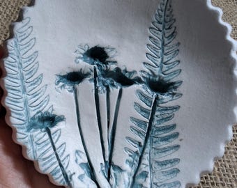 May include: A white ceramic dish with a scalloped edge features a blue fern and flower design.