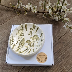 May include: A small white ceramic dish with a green floral design. The dish is sitting on a white box with a brown circle sticker that says "handmade with love".