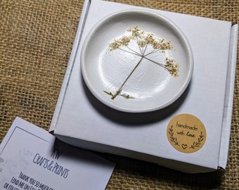 May include: A white ceramic trinket dish with a pressed dried flower design. The dish is packaged in a white box with a brown paper sticker that says "handmade with love".